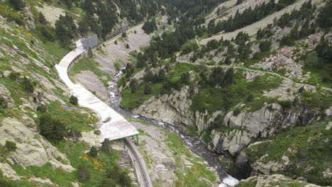 Aerial-Shot-Of-A-Mountainous-Landscape-In-Which-Railroad-Tracks-Run-Along-The-Side-Of-A-Rich-River-In-The-Pyrenees