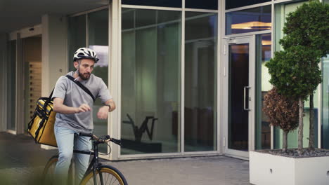 Food-Delivery-Guy-Wearing-Thermal-Backpack-Takes-A-Look-At-His-Smartwatch-To-Know-Where-To-Go-With-His-Bike