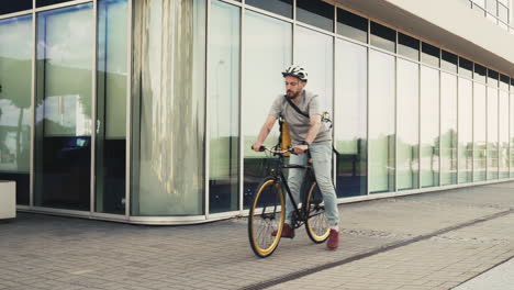 Food-Delivery-Man-Wearing-Thermal-Backpack-Stops-His-Bike-Next-To-An-Office-Building-To-Take-A-Look-At-His-Smartwatch-And-Make-Sure-It-Is-Headed-To-The-Exact-Delivery-Address
