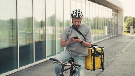 Food-Delivery-Guy-Wearing-Thermal-Backpack-Uses-The-Geolocator-On-His-Smartphone-To-Navigate-To-The-Delivery-Location-Riding-A-Bike
