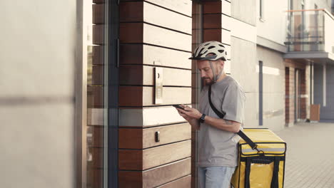Food-Delivery-Guy-Wearing-Thermal-Backpack-Parks-His-Bike-Next-To-The-Entrance-Of-A-Building-To-Make-A-Delivery-For-Clients-And-Customers