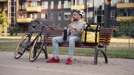 Food-Delivery-Rider-Man-Seated-On-A-Bench-Having-A-Cup-Of-Tea-During-His-Break