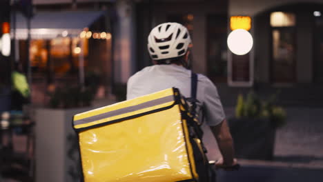 Food-Delivery-Courier-Wearing-Thermal-Backpack-Rides-A-Bike-At-Night-To-Deliver-Orders-For-Clients-And-Customers