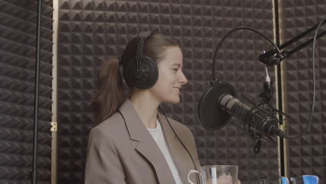 An-Elegant-Young-Woman-With-Her-Hair-Tied-Back-And-Wearing-A-Smiling-Suit-Listens-Smilingly-To-The-Person-Who-Is-Talking-In-A-Radio-Recording-Studio