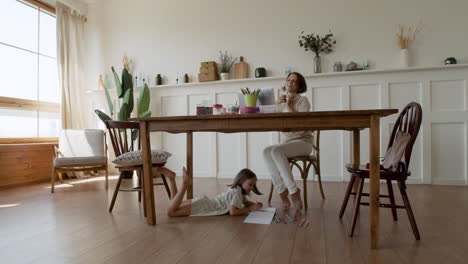 Wide-Shot-Of-A-Mother-Making-A-Videocall-While-Her-Daughter-Is-Distracted-Under-The-Table-Drawing-2