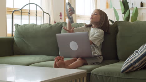 Ein-Verantwortungsbewusstes-Kleines-Blondes-Mädchen-öffnet-Den-Laptop-Und-Setzt-Ihre-Kopfhörer-Auf,-Um-Ihren-Online-unterricht-Von-Zu-Hause-Aus-Zu-Beginnen