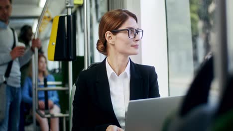 Young-Attractive-Businesswoman-In-Glasses-Going-Home-In-The-Tram-And-Working-On-The-Laptop-Computer-As-Being-Very-Busy