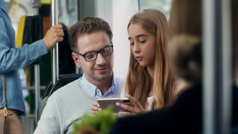 Close-Up-Of-The-Good-Looking-Man-In-Glasses-Going-In-The-Tram-With-His-Pretty-Cute-Teenage-Daughter-While-She-Showing-Him-Something-On-The-Smartphone