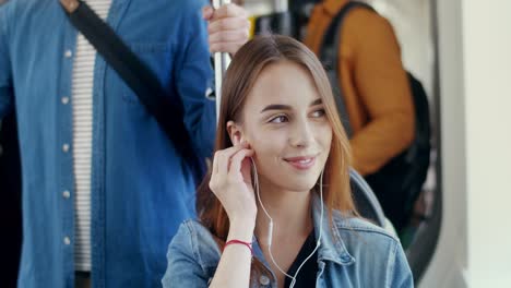 Close-Up-Of-The-Young-Attractive-Happy-Girl-Putting-Headphones-In-Ears-And-Listening-To-The-Music-On-The-Smartphone-While-Going-In-The-Tram