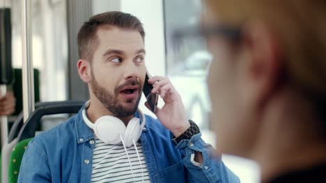Close-Up-Of-The-Blurred-Rear-Businesswoman-And-Young-Attractive-Happy-Guy-With-Big-Headphones-On-His-Neck-Talking-Cheerfully-On-The-Mobile-Phone-On-The-Background