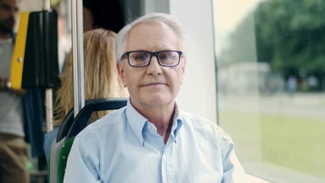 Porträt-Des-Gutaussehenden-älteren-Mannes-Mit-Brille,-Der-In-Die-Straßenbahn-Fährt,-Sitzt-Und-In-Das-Fenster-Schaut,-Der-In-Die-Kamera-Lächelt