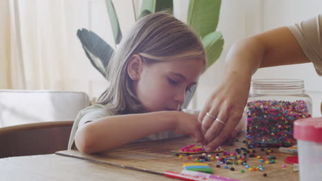 Close-Up-Of-A-Cute-Little-Blonde-Girl-Having-Fun-Playing-With-Colored-Beads-Helped-By-Her-Mother