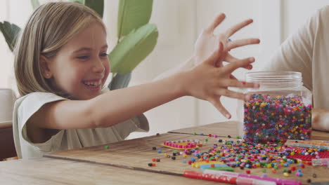 Close-Up-Of-A-Beautiful-Little-Blonde-Girl-Dropping-Colored-Beads-On-The-Table-And-Having-A-Great-Time