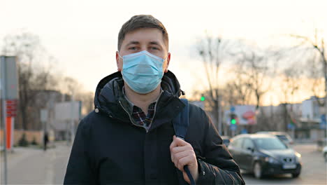 Portrait-Of-Handsome-Man-In-Medical-Mask-Standing-Outside-At-Street-With-Backpack-And-Turning-Face-To-Camera