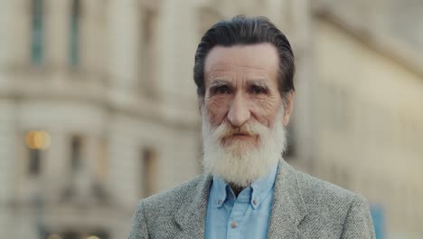 Portrait-Of-An-Elegant-Elderly-Man-With-A-White-Beard-And-Black-Hair-In-The-City-Looking-Straight-At-The-Camera