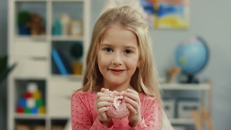 Portrait-Of-The-Beautiful-Sweet-Blonde-Little-Girl-Smiling-To-The-Camera-With-A-Pink-Donut-In-Hands-In-Her-Cozy-Room