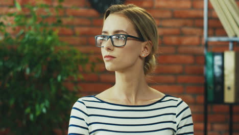 Portrait-Of-The-Beautiful-Young-Blonde-Woman-In-Glasses-And-Striped-Blouse-Turning-Her-Head-To-The-Camera-And-Smiling-Nice