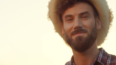 Portrait-Of-The-Smiled-Attractive-Young-Farmer-Taking-On-A-Hat-And-Looking-To-The-Camera-In-His-Margin-At-The-Dawn