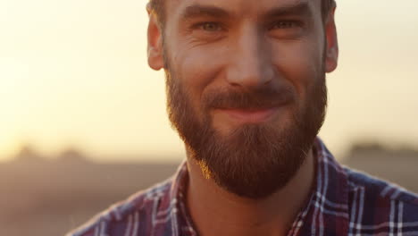 Close-Up-Of-The-Good-Looking-Young-Man-With-A-Beard-Smiling-To-The-Camera-And-Then-Looking-Down-Early-In-The-Morning-At-His-Field