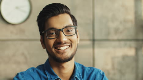 Close-Up-Portrait-Of-Joyful-Office-Worker-With-Glasses-Smiling-To-Camera-While-Sitting-At-Table-At-Workplace