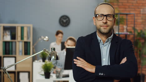 Portrait-Shot-Of-The-Handsome-Businessman-Ib-Glasses-And-Official-Style-Standing-In-The-Office-Room,-Leaning-On-The-Table-And-Turning-Head-To-The-Camera