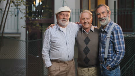 Portrait-Of-The-Three-Old-Men-Standing,-Hugging-And-Smiling-To-The-Camera-In-Front-Of-The-Camera-At-The-House