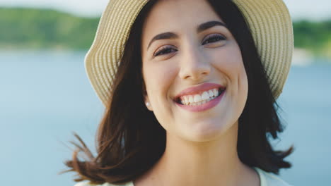 Portrait-Of-The-Beautiful-Brunette-Young-Woman-In-The-Hat-Smiling-Cheerfully-On-The-Lake-Background