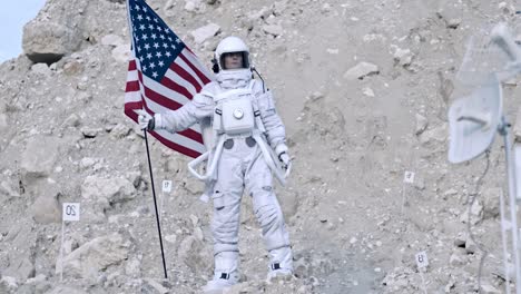 Woman-Astronaut-In-A-Space-Suit-Holds-A-Us-Flag-While-Looking-Around-Her-On-An-Unknown-Planet
