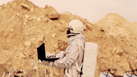Cosmonaut-In-The-Space-Costume-Standing-On-The-Mars-And-Trying-To-Catch-Wi-Fi-Connection-On-The-Laptop-Computer-While-Tapping-On-The-Keyboard-And-Doing-Researches