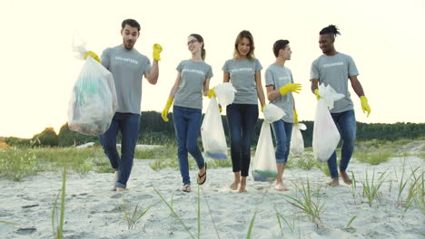 Group-Of-Young-Multiethnical-People-Walking-The-Beach-With-Plastic-Bags-Full-Of-Garbage