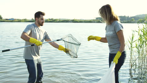 Man-And-Woman-Volunteering-While-Collecting-Garbage-From-A-Lake-Bottom-With-A-Special-Steel-Net