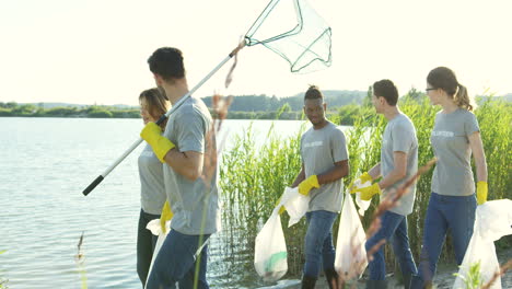 Environmental-Young-Mixed-Races-Volunteers-Walking-At-The-Lake-Bank-With-Plastic-Bags-Full-Of-Trash-And-Talking-After-Working-As-Cleaners