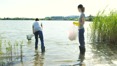 Ein-Paar-Freiwillige-Sammeln-Müll-Vom-Seegrund-Und-Sammeln-Ihn-In-Der-Plastiktüte,-Während-Sie-Den-See-Reinigen