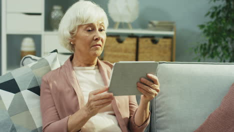 ältere-Grauhaarige-Frau,-Die-Einen-Videochat-Auf-Dem-Tablet-gerät-Per-Webcam-Im-Schönen-Wohnzimmer-Hat