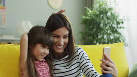 Nahaufnahme-Der-Lächelnden-Mutter-Und-Tochter,-Die-Ein-Lustiges-Selfie-Auf-Dem-Smartphone-Auf-Der-Gelben-Couch-Machen