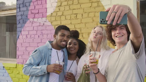Group-Of--Young-Friends-Taking-Selfies-Together-And-Having-Fun-Outdoors,-While-Holding-Their-Fresh-Drinks-In-Plastic-Cups