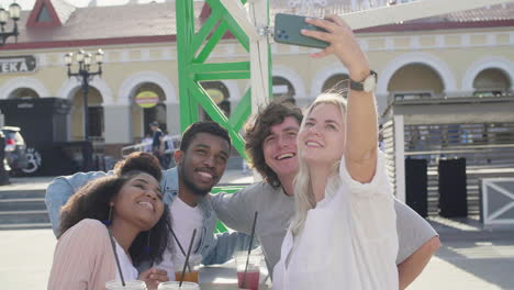 Group-Of-Cheerful--Young-Friends-Taking-Selfies-And-Having-Fun-Together,-While-Standing-At-The-Table-And-Eating-Pizza-In-The-Street