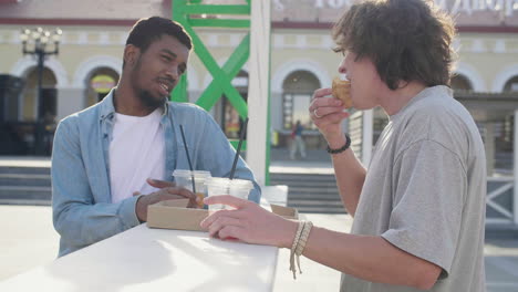 -Male-Friends-Chatting-While-Eating-Pizza-And-Drinking,-Standing-At-An-Outdoor-Table-In-The-Street