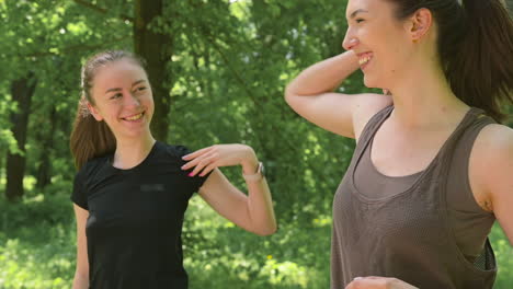 Two-Happy-Pretty-Female-Runners-Warming-Up-And-Streching-Their-Shoulders-In-The-Park