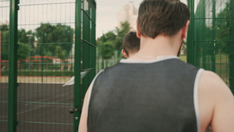 Two-Male-Basketball-Players-Walking-Together-And-Talking-Each-Other,-While-Entering-In-An-Outdoor-Basketball-Court