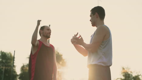 Male-Basketball-Players-Stretching-Arms-And-Shoulders-In-An-Outdoor-Basketball-Court-While-Talking-Each-Other