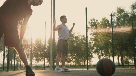 Concentrated-Male-Basketball-Players-Stretching-In-Outdoor-Basketball-Court-At-Sunset
