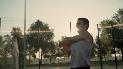 Concentrated-Sportsman-Doing-Deltoid-And-Tricep-Stretch-Exercises-In-Outdoor-Court-At-Sunset