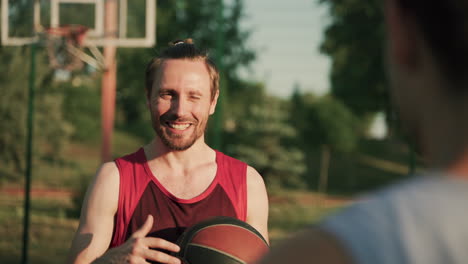 Portrait-Of-A-Smiling-Handsome-Basketball-Player-Holding-A-Ball-And-Explaining-Something-To-His-Friend,-Standing-In-Front-Of-Him-In-Blurred-Foreground