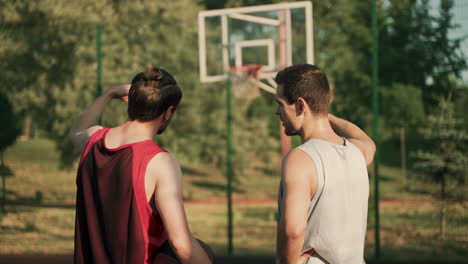 Back-View-Of-Two-Handsome-Male-Basketball-Players-Looking-At-Basket-And-Talking-About-Game-Tactics-In-A-Blurred-Outdoor-Basketball-Court-In-A-Sunny-Day