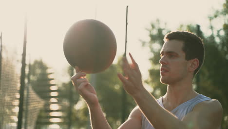 Ein-Konzentrierter-Basketballspieler,-Der-Versucht,-Bei-Sonnenuntergang-Auf-Einem-Basketballplatz-Im-Freien-Den-Ball-Auf-Seinem-Finger-Zu-Drehen