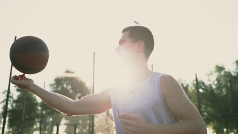 A-Smiling-Basketball-Player-Trying-To-Spin-Ball-On-His-Finger-In-An-Outdoor-Basketball-Court-At-Sunset