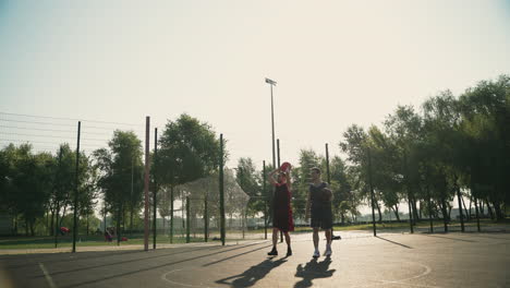 Two-Male-Basketball-Players-Walking-In-An-Outdoor-Basketball-Court,-While-Chatting-Together-And-One-Of-Them-Throwing-The-Ball