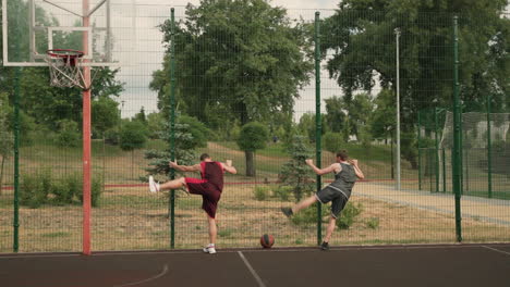 Two-Male-Basketball-Players-Stretching-Their-Legs,-Standing-And-Leaning-Against-A-Metal-Fence-In-An-Outdoor-Basketball-Court