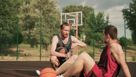 Two-Male-Basketball-Players-Taking-A-Break-And-Talking-To-Each-Other-During-Their-Training-Session-In-An-Outdoor-Basketball-Court
